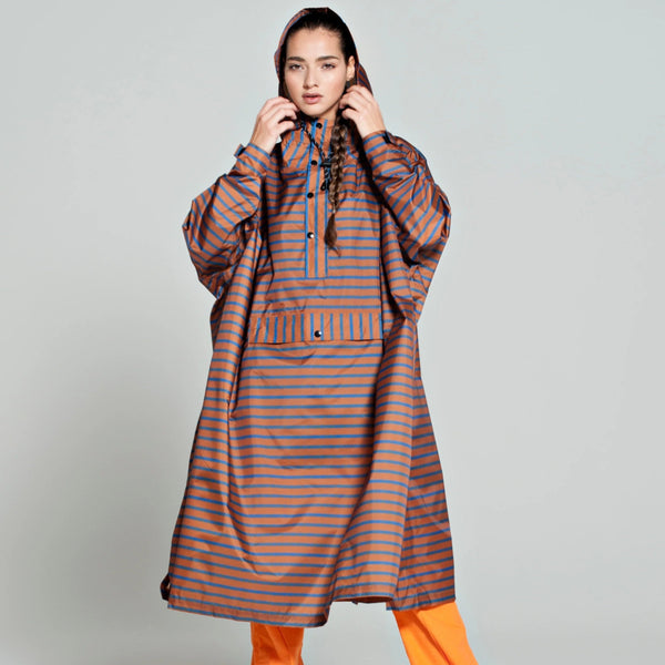 Person wearing a long, striped raincoat with orange pants on a plain background