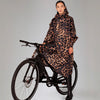 Person wearing a leopard print raincoat standing next to a bicycle on a plain background