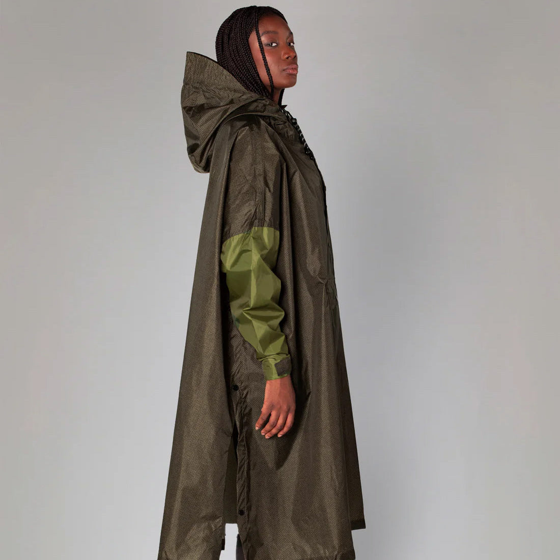 Person wearing a long olive green raincoat with a hood on a plain background